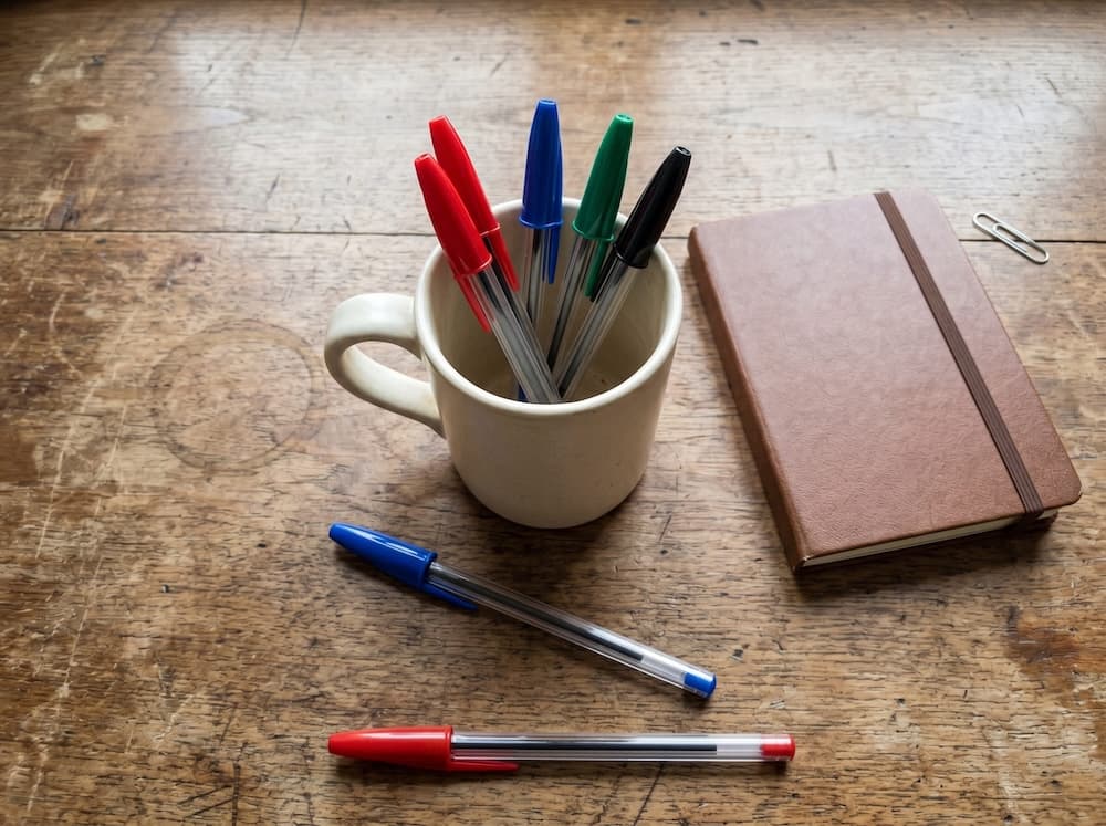 Desk scene with a mug, pens on the desk, and nearby objects — count-and-locate benchmark