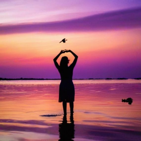 A woman standing in the water with a bird flying above her head