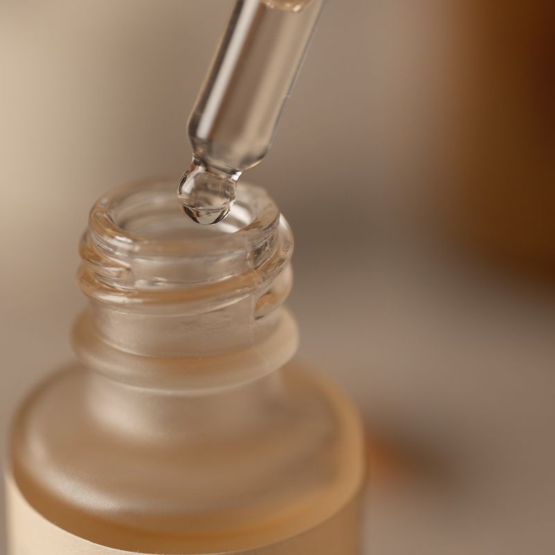 Extreme close-up of the neck and pipette of the serum bottle with a bead of serum hanging from the glass