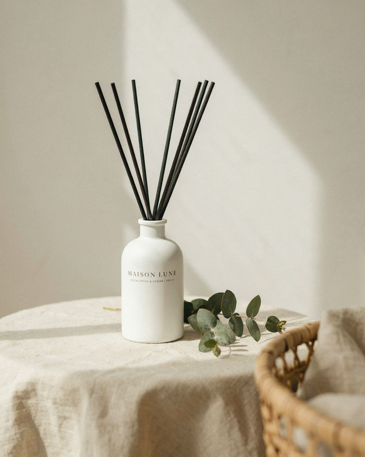 A white ceramic reed diffuser on a linen-draped side table, filling the middle of the frame