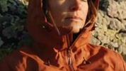 A soft, blocky close crop of the hiker's face and the collar of her burnt orange jacket, the fabric weave smeared into flat colour