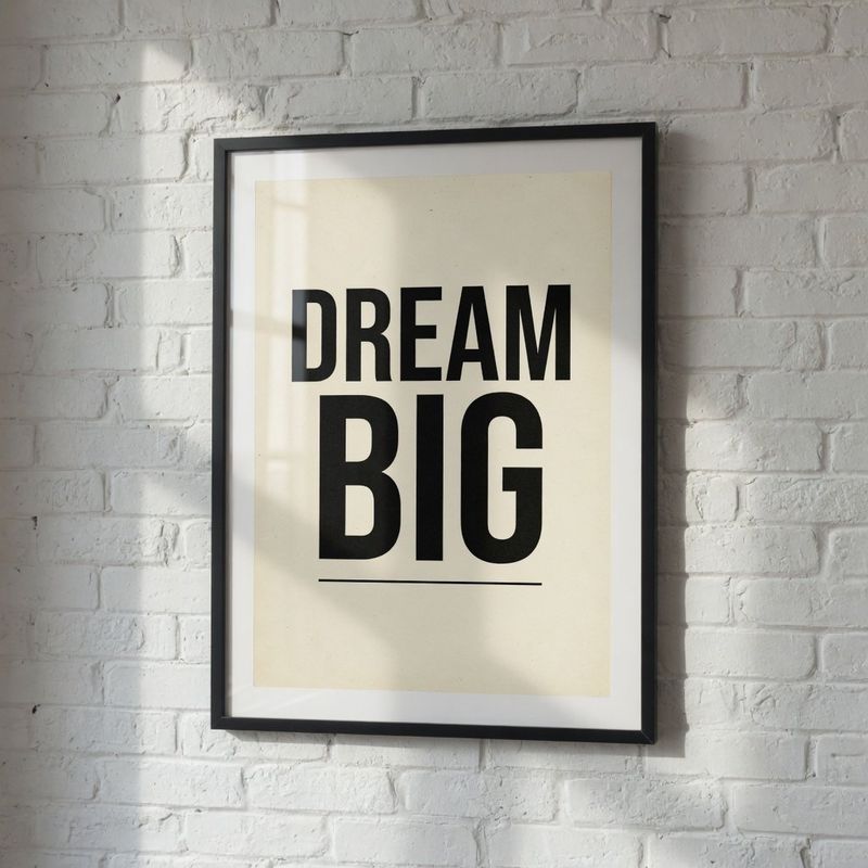 A framed motivational poster on a white brick wall reading DREAM BIG in bold black letters
