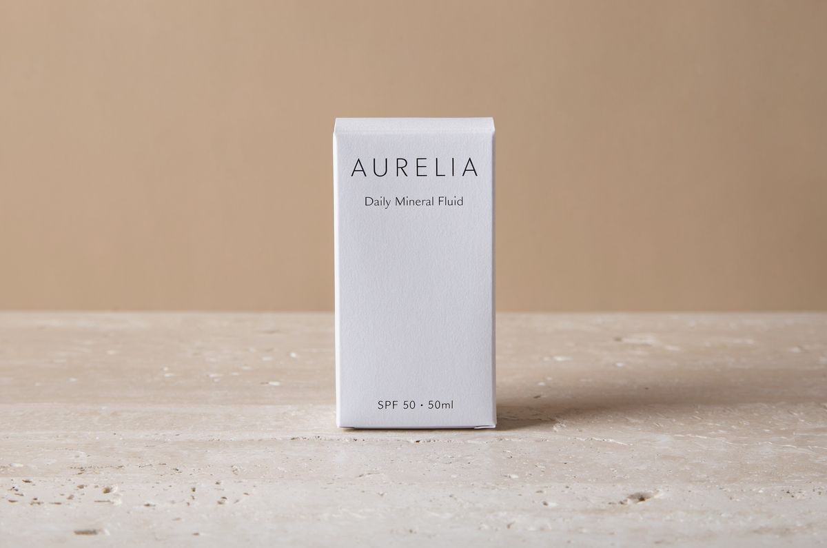 A matte white skincare carton reading AURELIA in letterspaced capitals, Daily Mineral Fluid below it, and SPF 50 50ml along the bottom edge