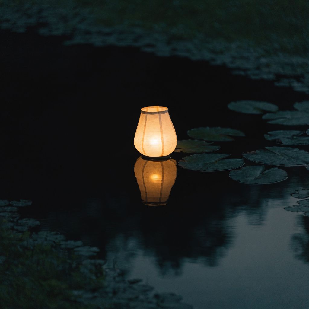 A glowing paper lantern resting on the dark surface of a night pond