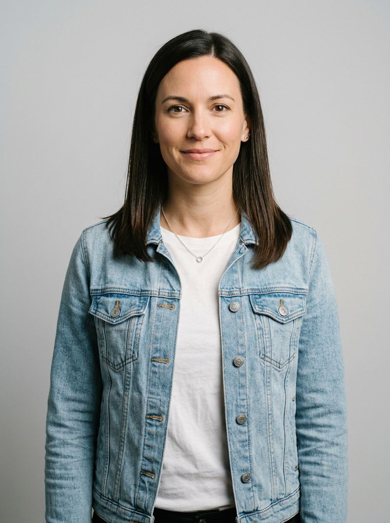 A woman with straight dark-brown hair in a plain light-wash denim jacket, front view on a light-gray background