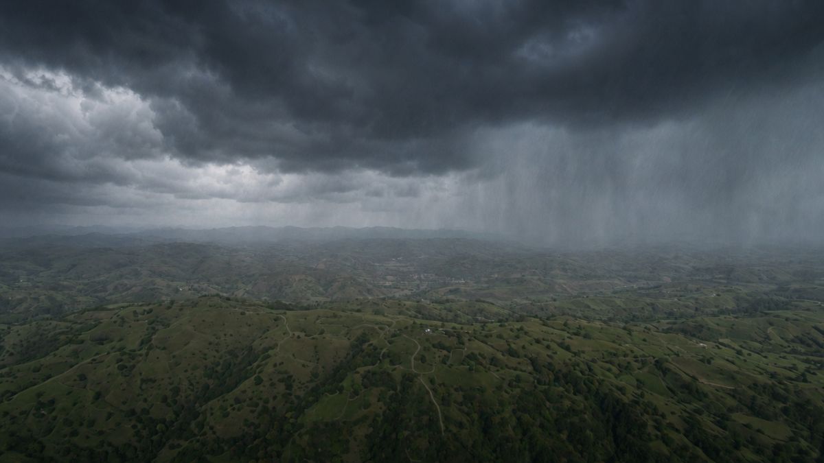 Rolling green hills under a dark stormy sky with sweeping rain