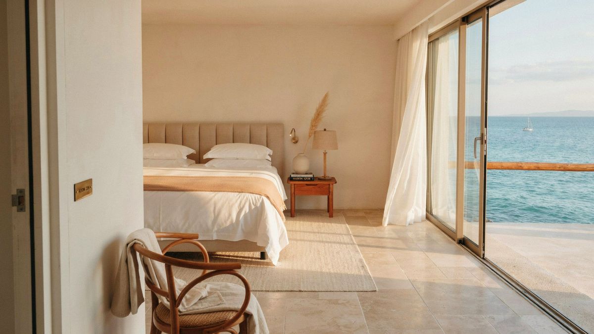 A hotel room seen from the doorway, with a rattan chair, a bed and glass doors open to the sea, generated with Magic Prompt on auto