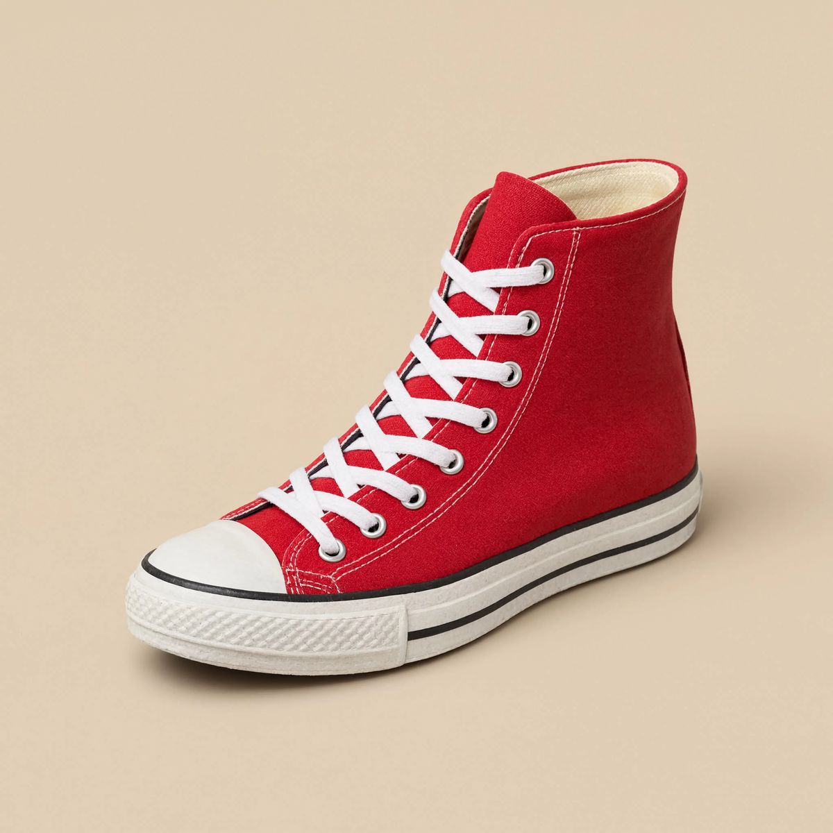 A single bright red high-top canvas sneaker with a white rubber sole standing at a three-quarter angle on a warm cream studio backdrop