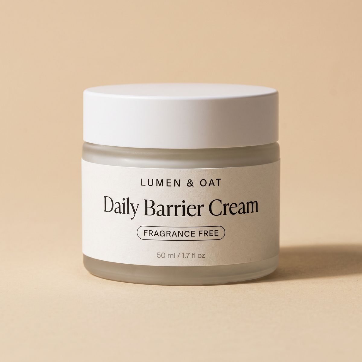 A frosted glass jar with a white lid on a sand backdrop, its label reading LUMEN & OAT in small spaced capitals, Daily Barrier Cream in a large serif, FRAGRANCE FREE inside an outlined pill, and 50 ml / 1.7 fl oz in tiny gray type at the bottom