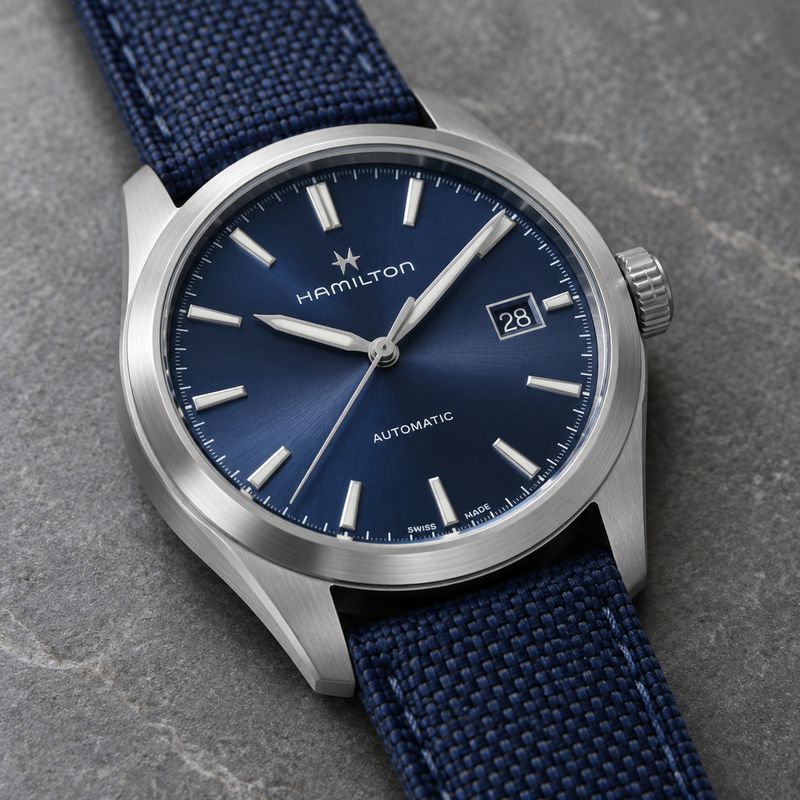 A stainless steel automatic wristwatch with a navy sunburst dial on a grey stone surface, shot at a three-quarter angle