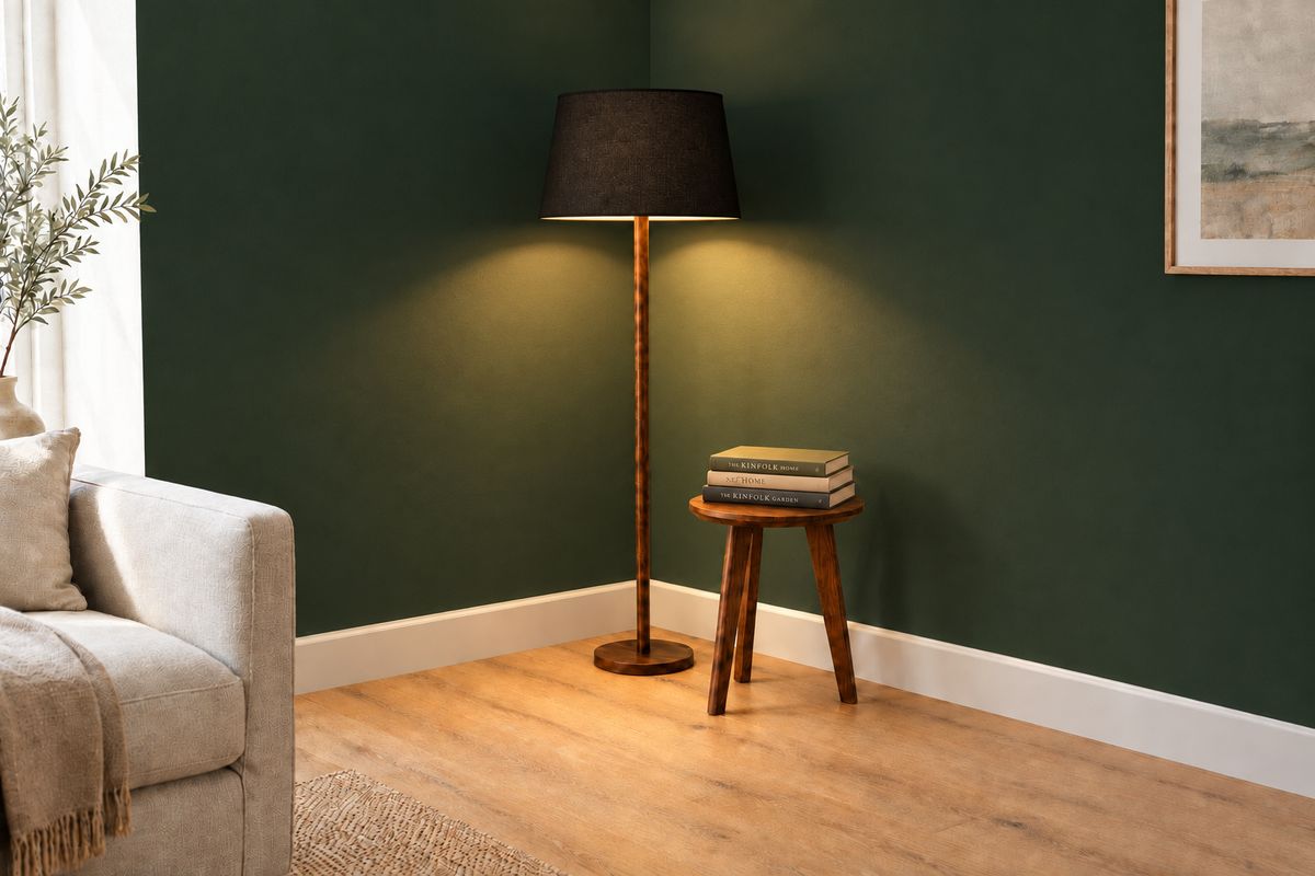 The same corner with the lamp switched on, warm light falling down the green wall and across the side table and the stack of books