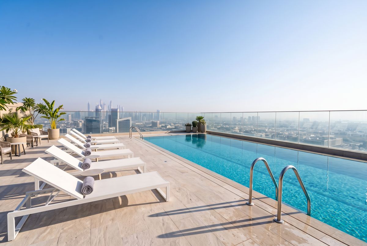 The same pool deck with the wet-floor sign and the striped towel gone, clean stone tiles by the steps and a bare white cushion on the nearest lounger