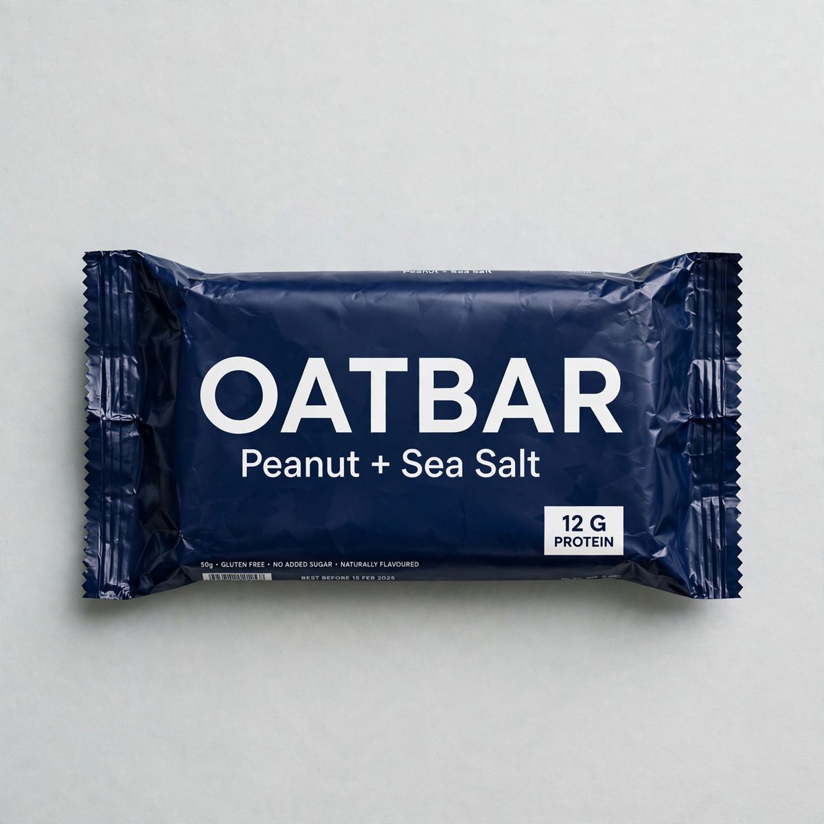 A flat lay of a deep navy protein bar wrapper printed with OATBAR in large white capitals, Peanut + Sea Salt beneath it, and 12 G PROTEIN in a small white box in the lower right corner