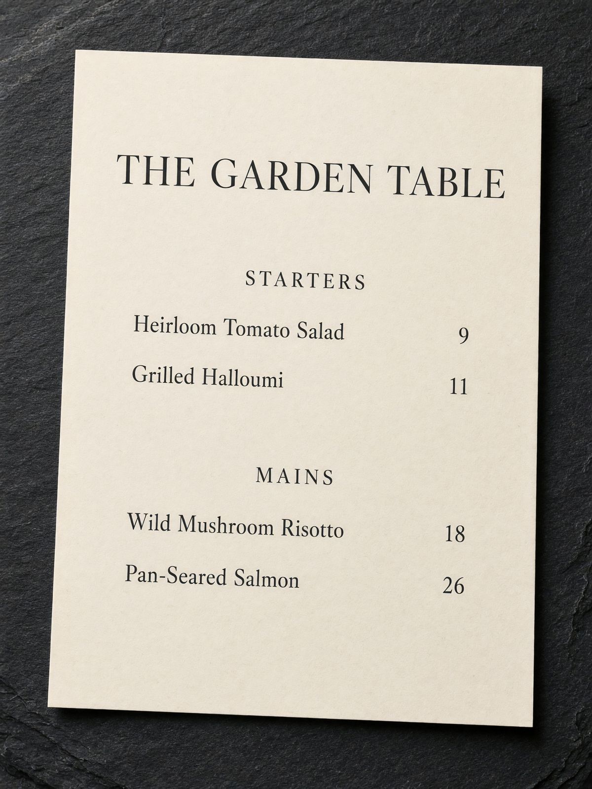 A printed restaurant menu headed THE GARDEN TABLE with a STARTERS section listing Heirloom Tomato Salad and Grilled Halloumi and a MAINS section listing Wild Mushroom Risotto and Pan-Seared Salmon, each with prices