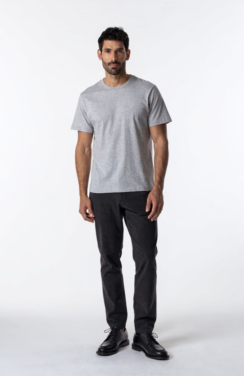 A full-body studio photo of a man in a plain grey t-shirt and dark trousers on a white background