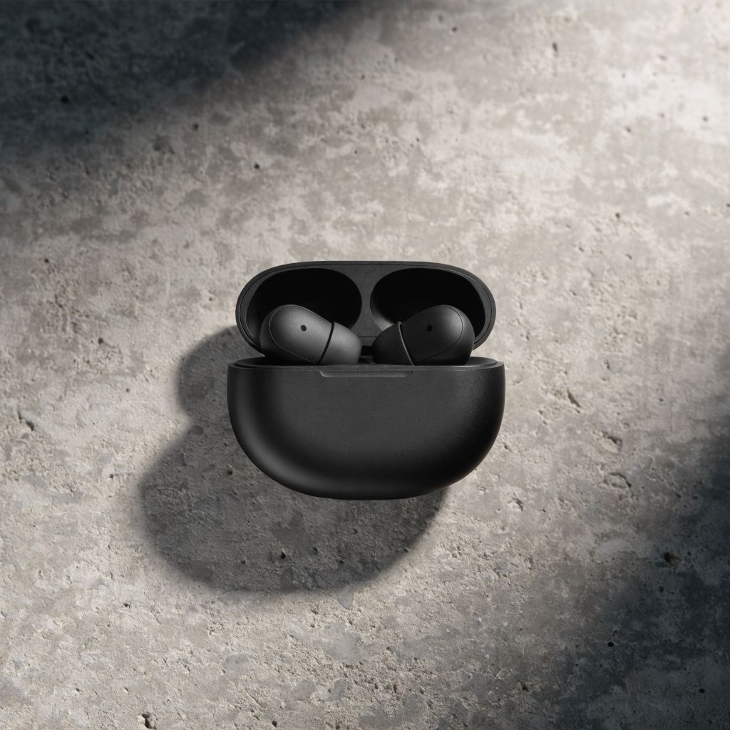 A pair of wireless earbuds in a matte black charging case on a concrete surface