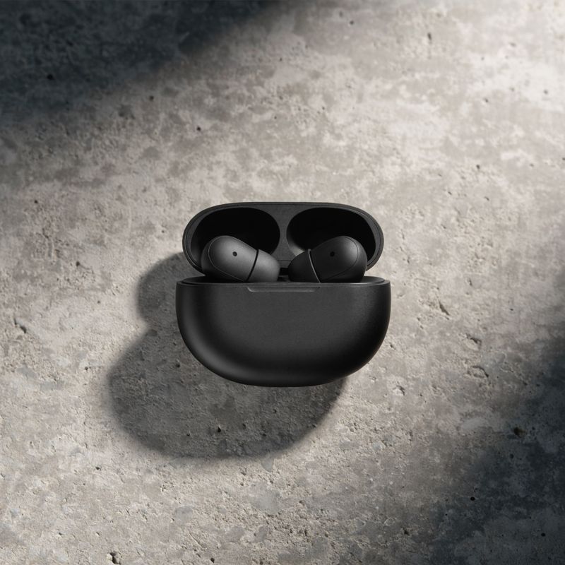 A pair of wireless earbuds in a matte black charging case on a concrete surface