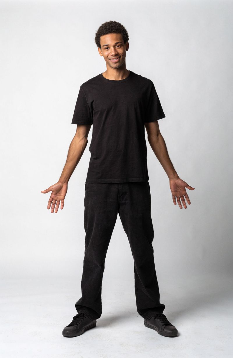A man facing the camera in a relaxed, open standing pose with his arms loose at his sides