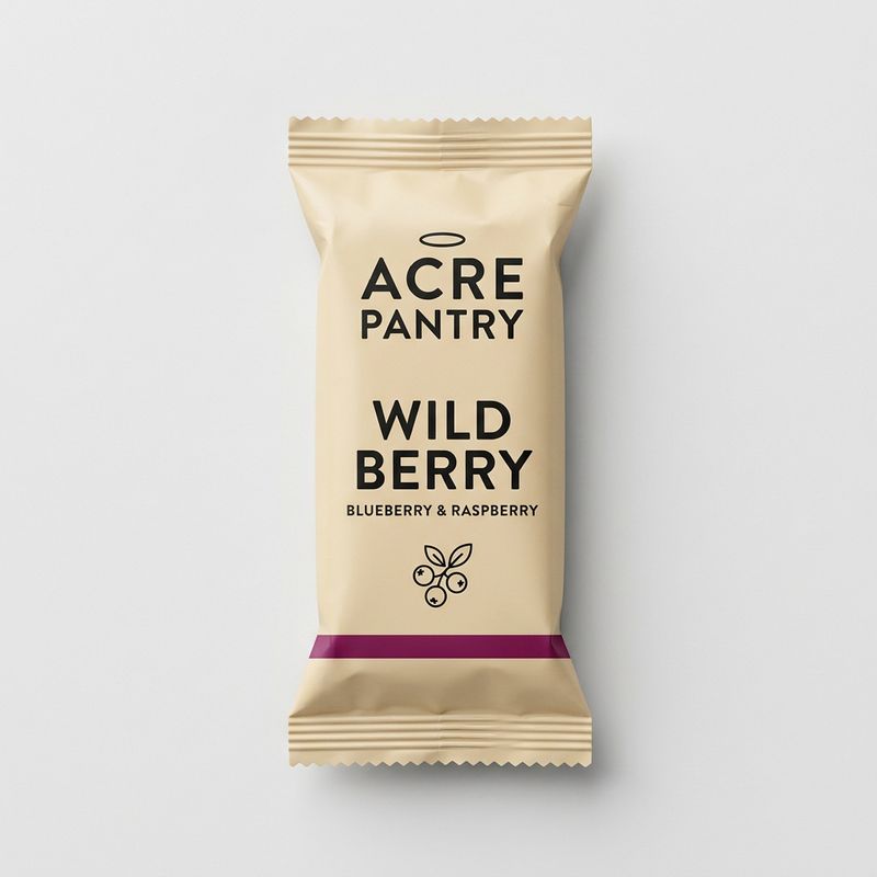 Flat-lay product photograph of the Acre Pantry Wild Berry granola bar in a flow-wrap pillow pouch, kraft cream paper with ACRE PANTRY wordmark, WILD BERRY flavor name, berry sprig illustration, and berry purple accent stripe
