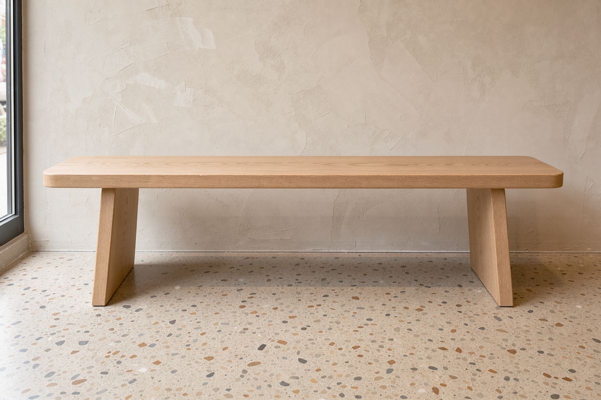 An empty pale oak bench against a lime-washed plaster wall on a terrazzo floor