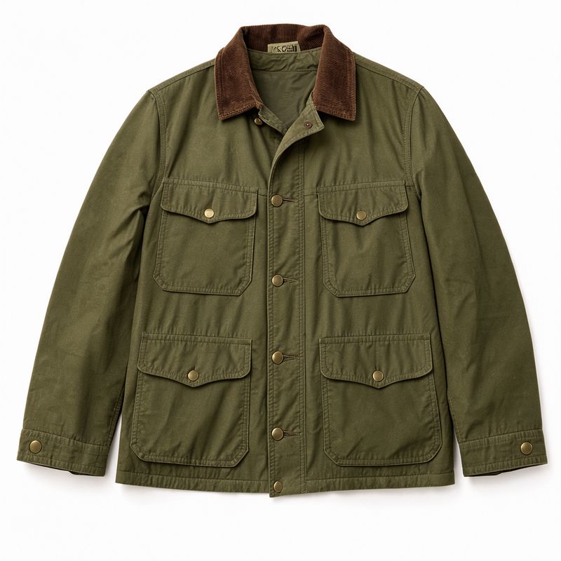 An olive waxed cotton field jacket with a brown corduroy collar and four flap pockets laid flat on white