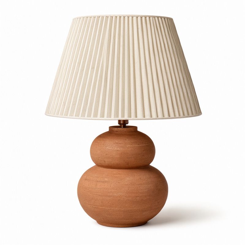 A table lamp with a ribbed terracotta gourd-shaped base and a pleated off-white linen shade on a white background