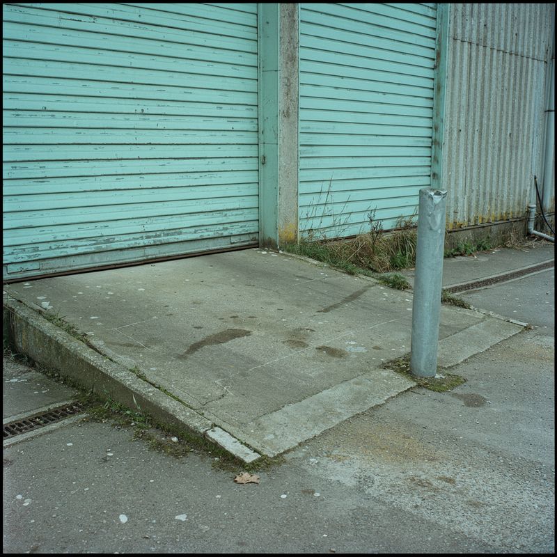 An empty loading bay with pale teal corrugated shutters and a concrete ramp