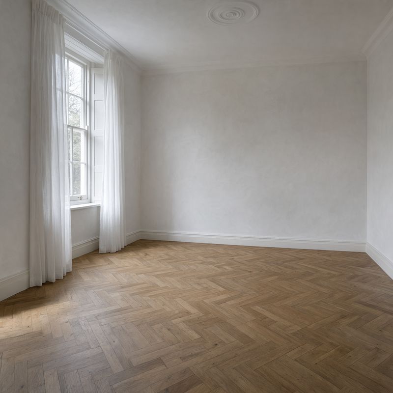 An empty living room with white walls, herringbone oak floor and a tall sash window