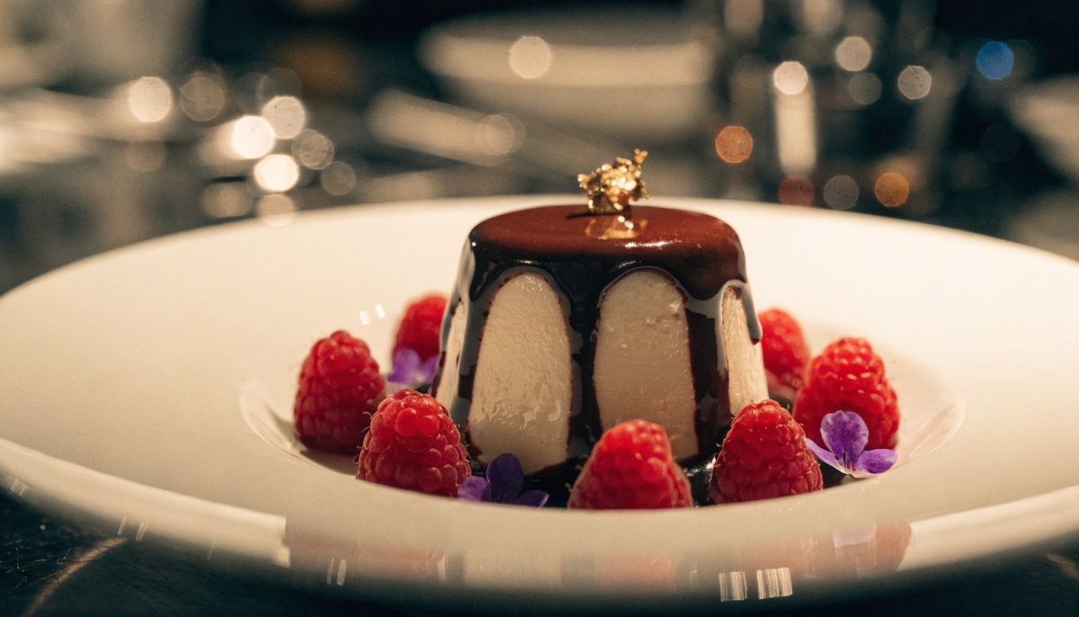 A close beauty shot of the finished plated dessert with chocolate, raspberries, and a piece of gold leaf catching the light