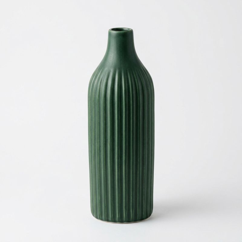 A studio photo of a tall ribbed ceramic vase in deep forest green with a matte glaze and narrow neck on a white background