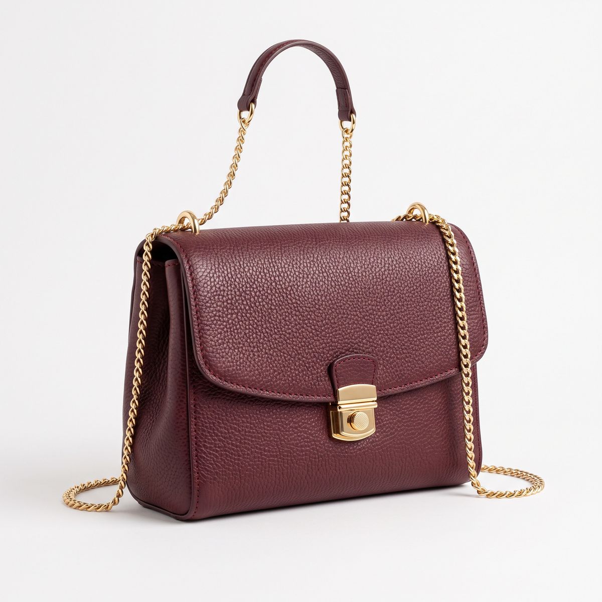 A burgundy pebbled-leather crossbody bag with a gold chain strap on a white background