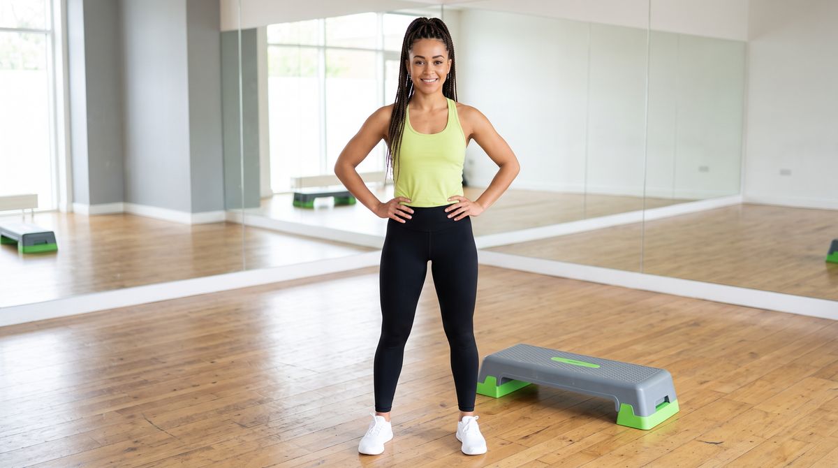 A full-length photo of a fitness instructor with high braids in a lime-green top and black leggings beside an aerobic step in a mirrored studio