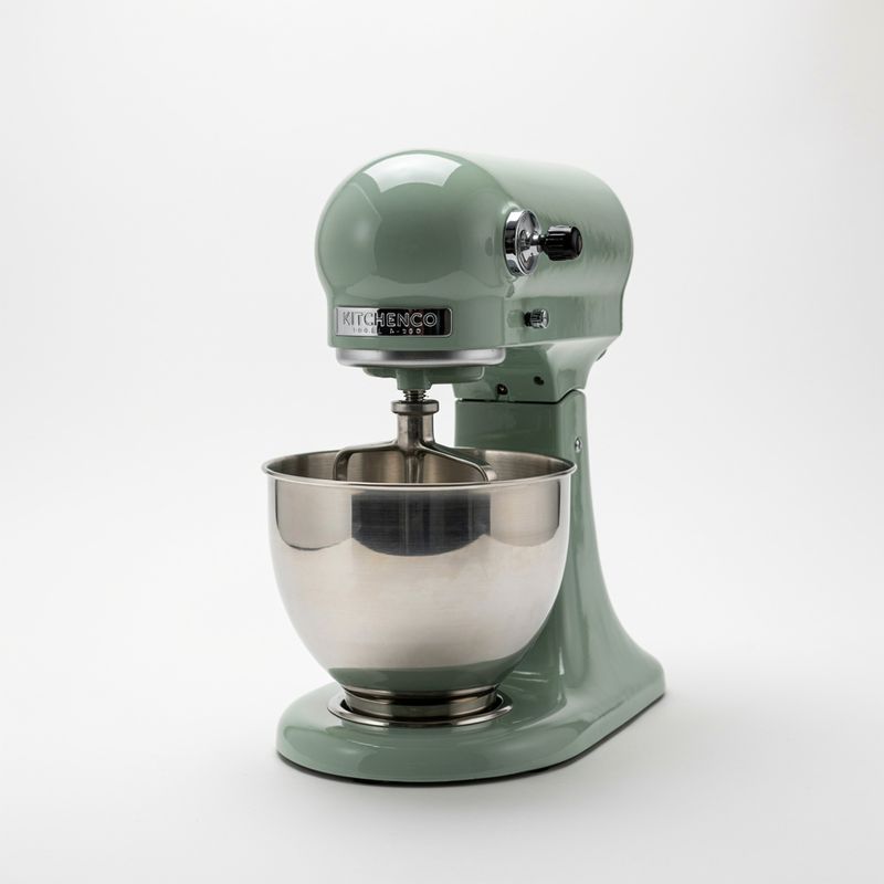 A glossy sage green stand mixer with a steel bowl on a white background