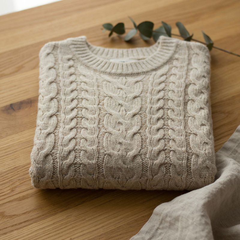 A folded oatmeal cable-knit sweater at 1K, with a magnified inset of the cable pattern