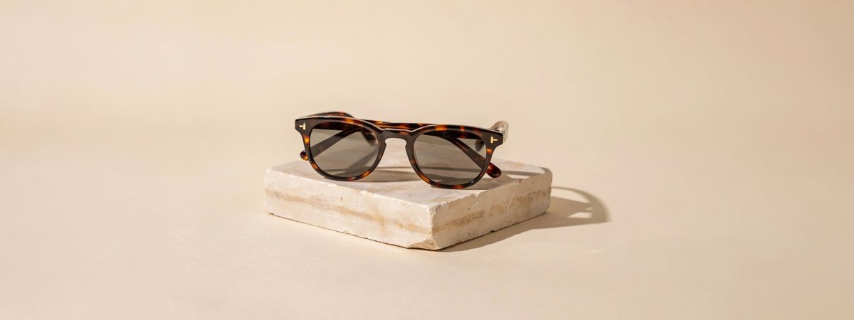 The sunglasses on a sandstone block extended into a wide banner, with warm beige background on both sides