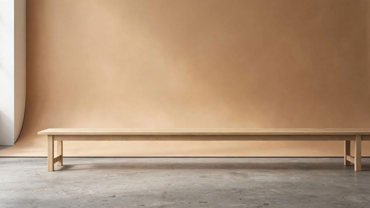 An empty studio set with a warm sand-coloured seamless backdrop, a long pale oak bench and a bare concrete floor