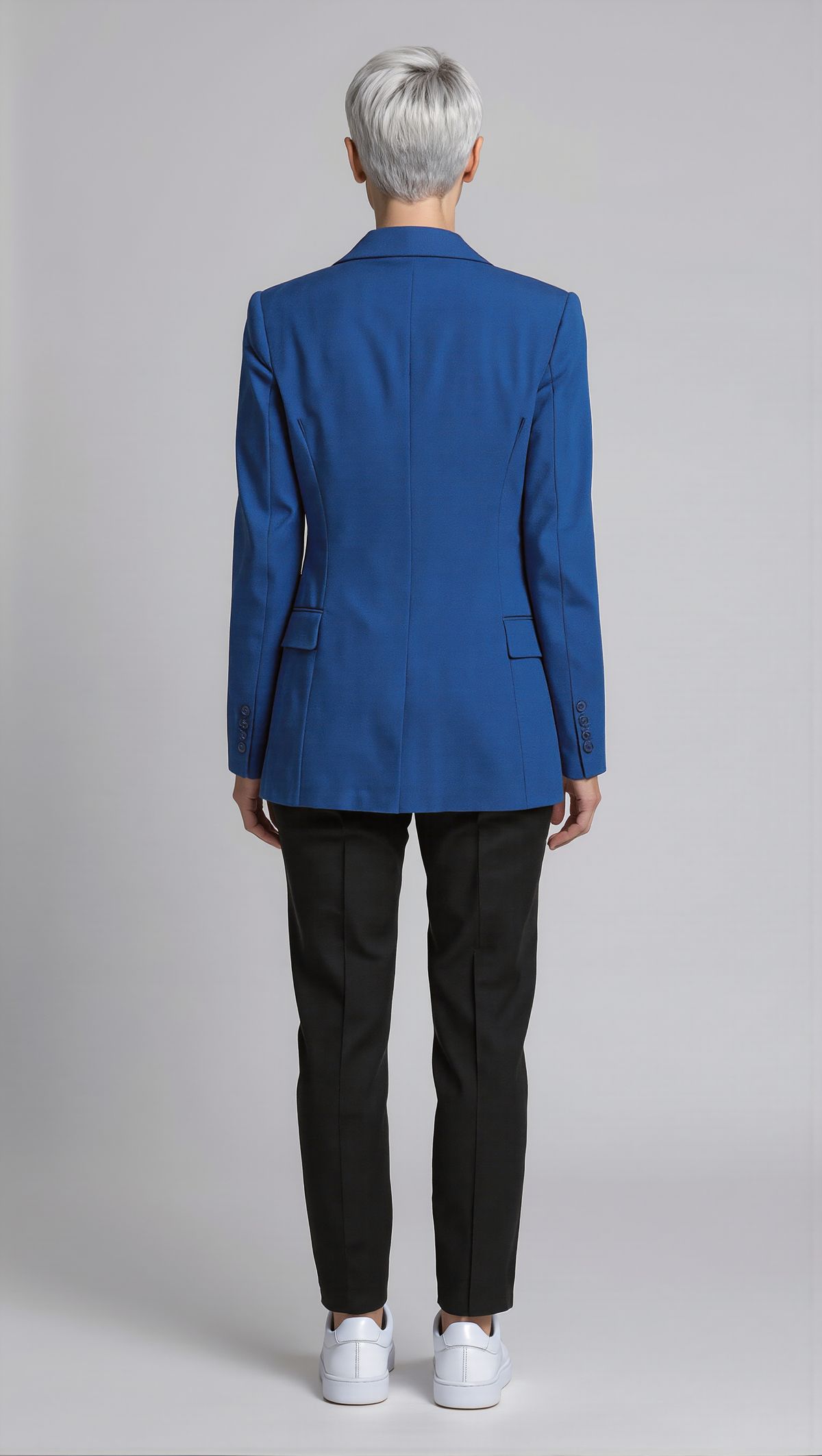 The same woman seen from behind, showing the back of her silver pixie cut and cobalt blazer