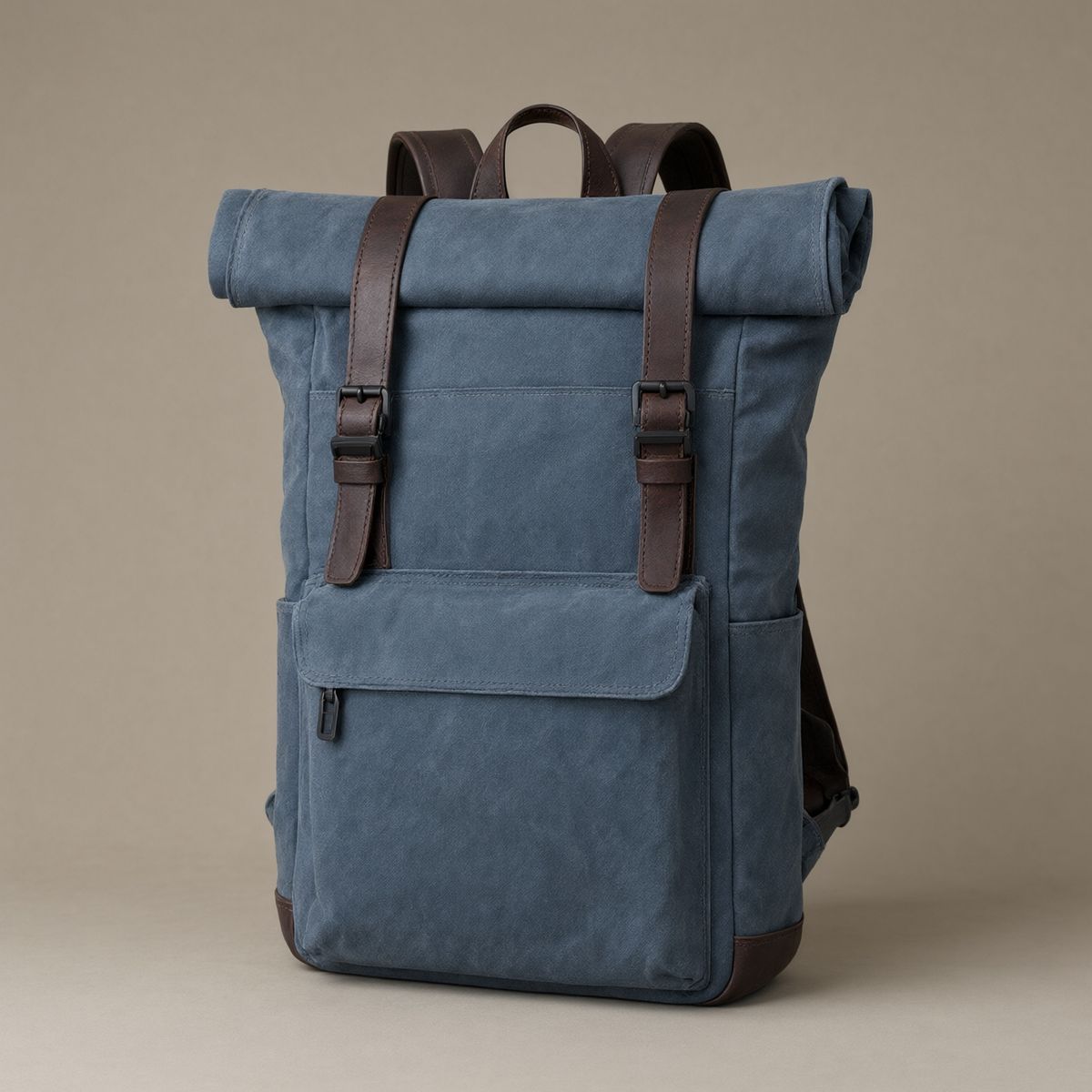 A slate blue waxed canvas roll-top backpack with dark brown leather straps on a plain warm grey backdrop