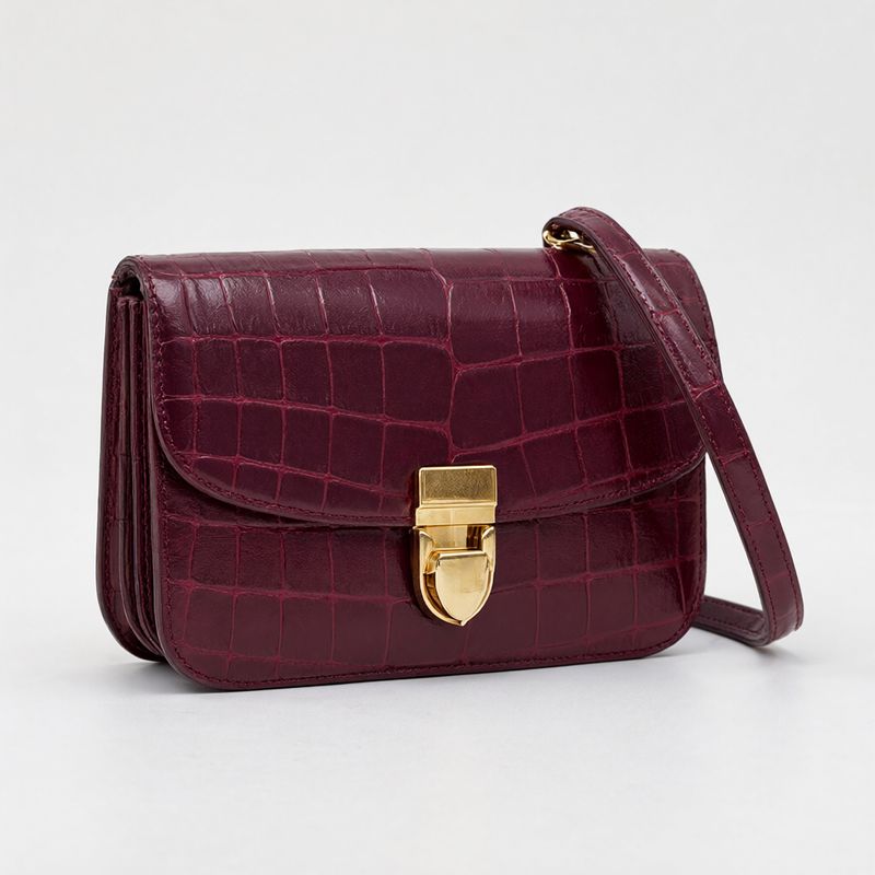 A small burgundy croc-embossed leather shoulder bag with a gold clasp on white