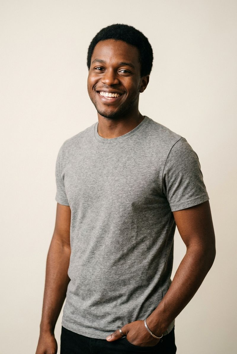 A studio portrait of a man in his mid-twenties with close-cropped hair and a heather-grey graphic tee, smiling