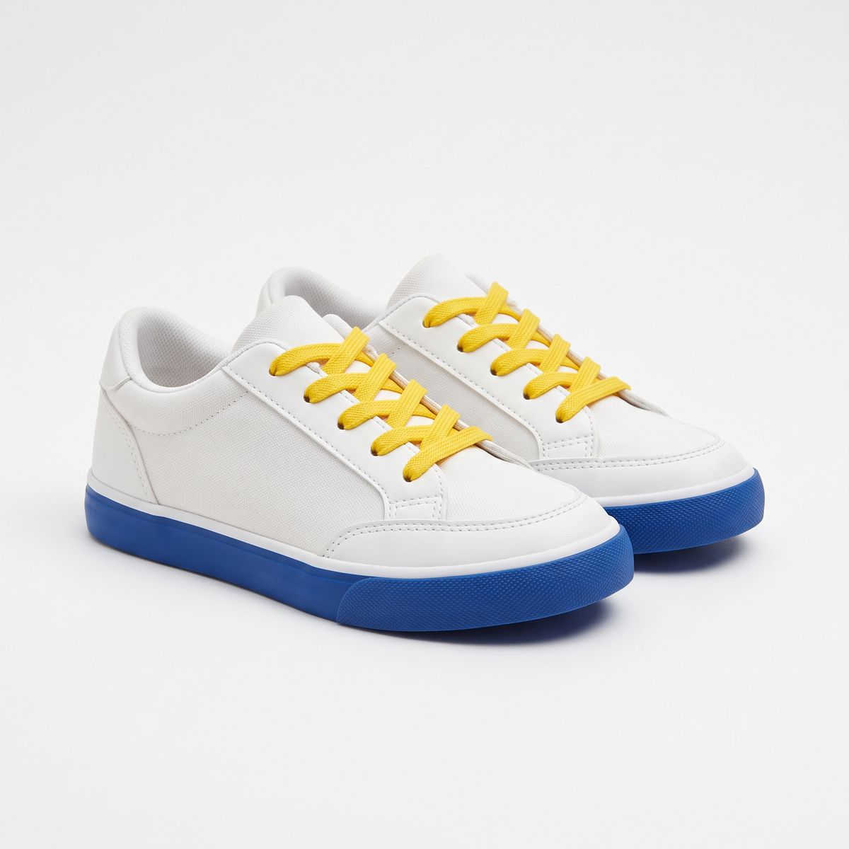 A pair of kids' white sneakers with cobalt blue soles and yellow laces on white