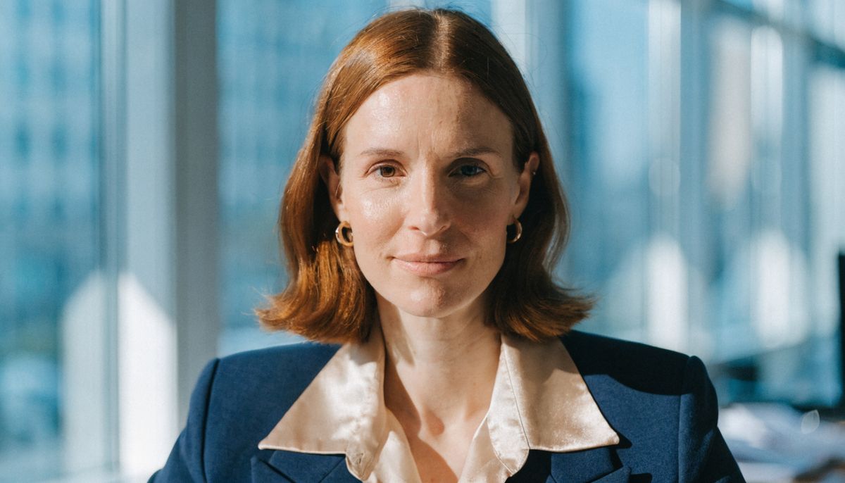 Auburn-haired businesswoman in a navy blazer facing the camera, head and shoulders framing