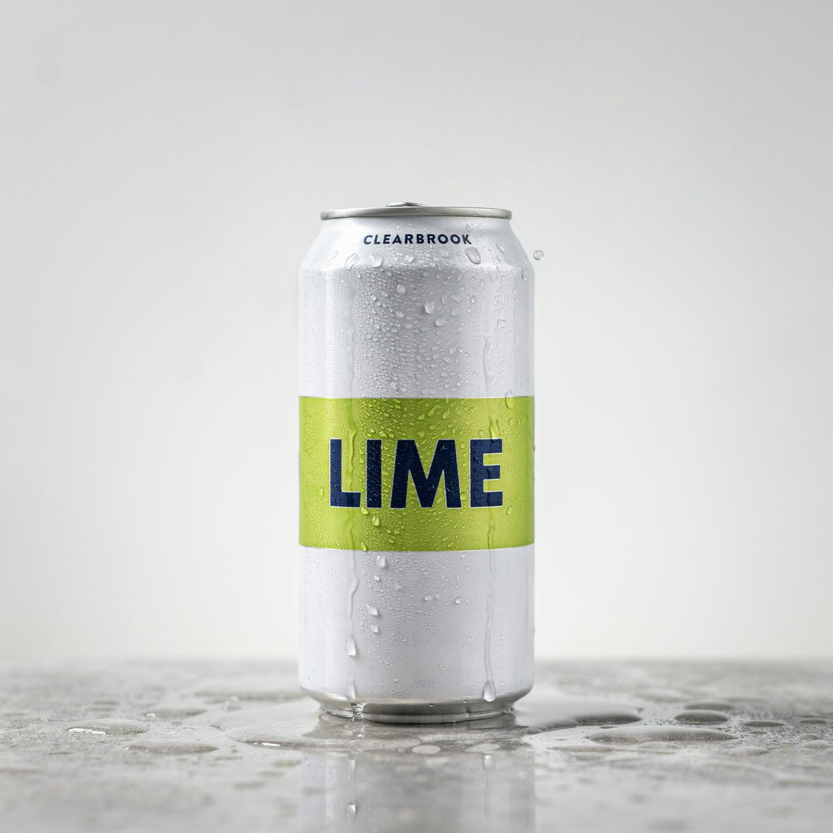 A white sparkling water can with a lime green band reading LIME, and CLEARBROOK near the top, on a wet gray stone surface
