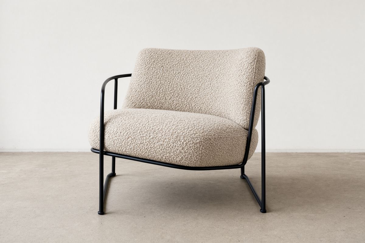 A lounge chair upholstered in oatmeal boucle with a black steel frame on a pale concrete floor