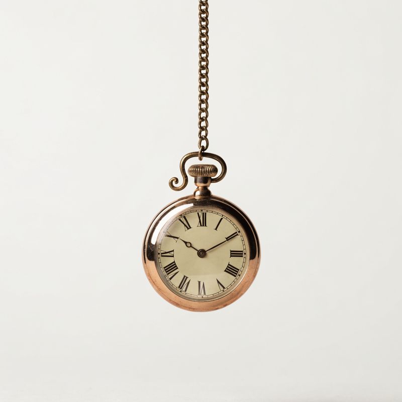 A rose-gold antique pocket watch with an ivory Roman-numeral dial on an off-white background