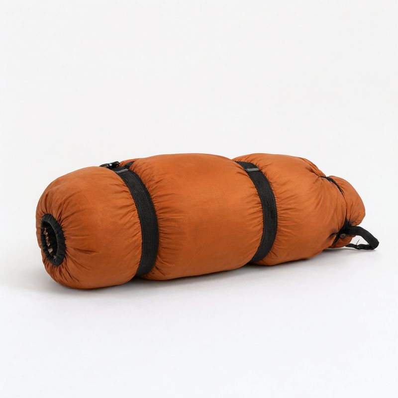 A rolled burnt orange sleeping bag cinched with two black straps on white
