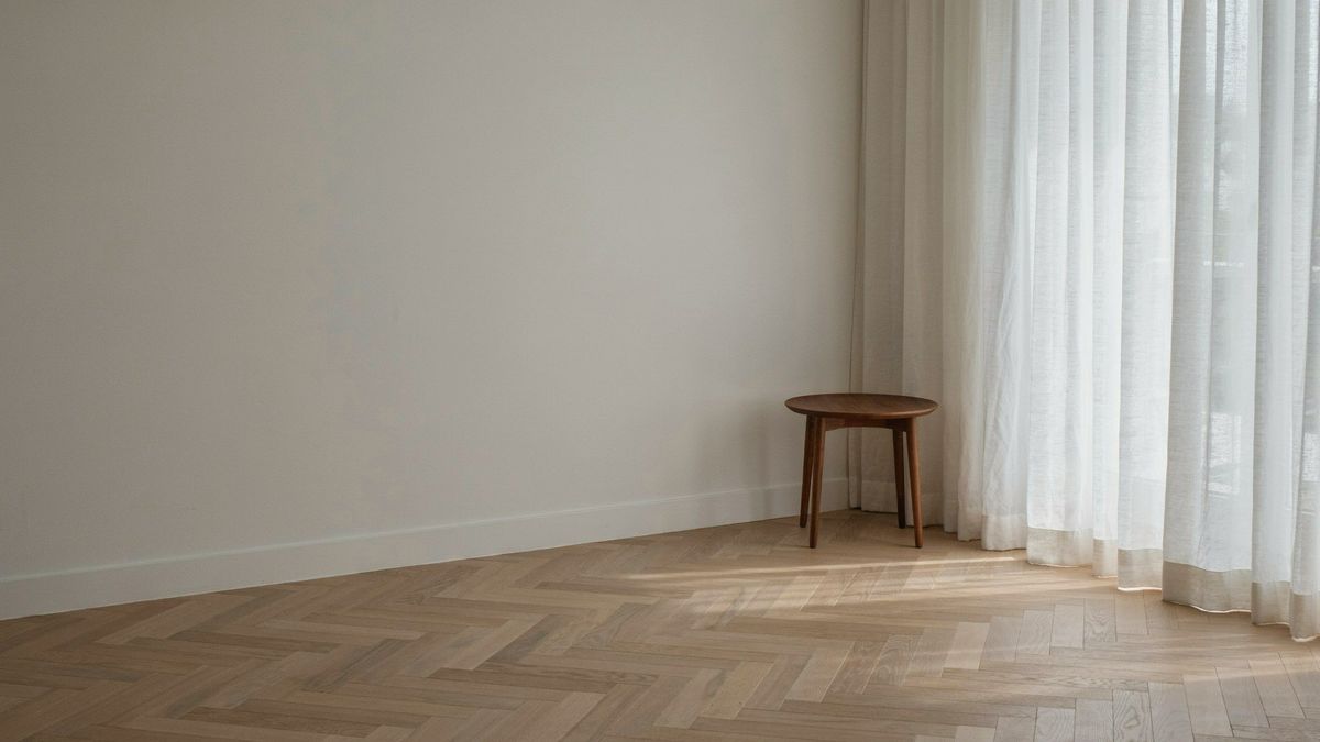 A living room corner with a large curtained window, a pale oak floor and an empty space by the window