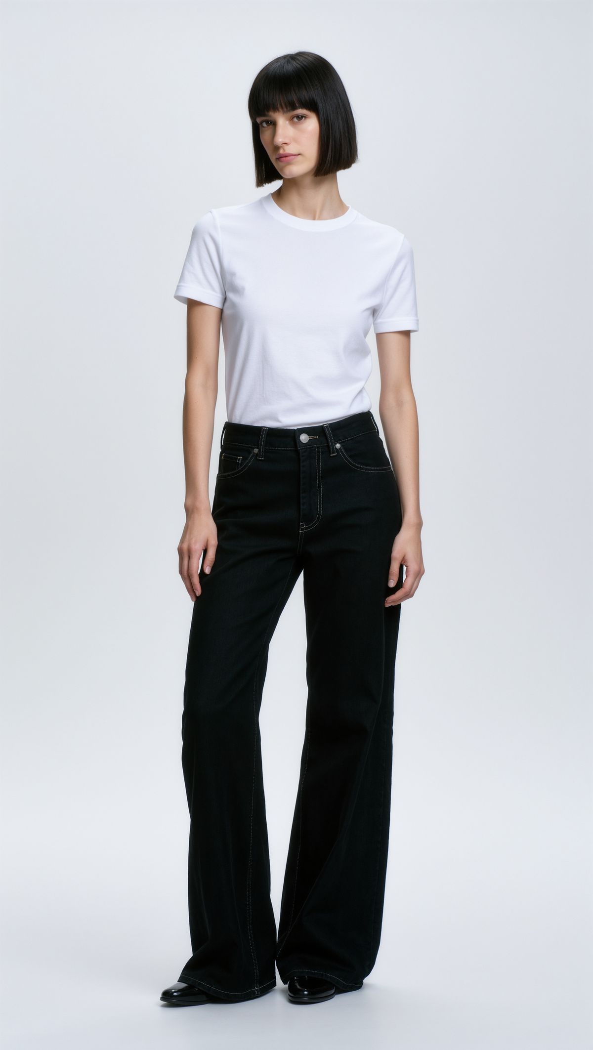 Full-length studio portrait of a model with a dark bob in a white t-shirt and black jeans against a light gray backdrop