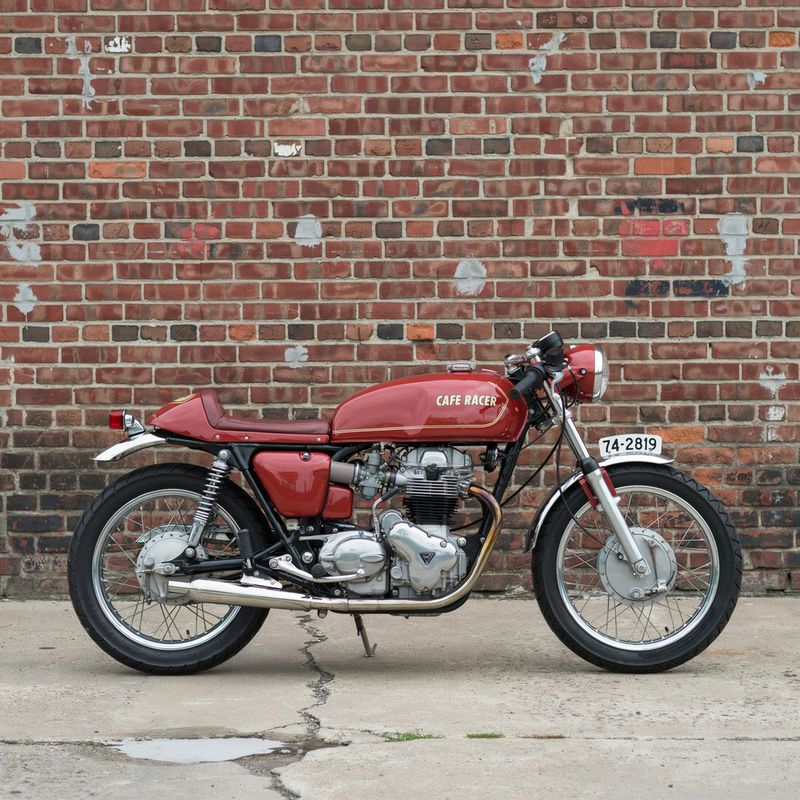 A vintage cafe-racer motorcycle parked side-on against a weathered red-brick wall