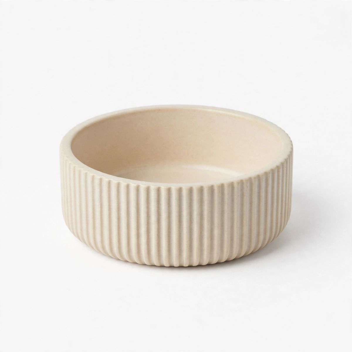 A small round ribbed ceramic dish in warm off-white, empty, on a white background